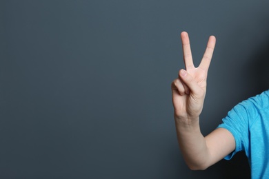 Photo of Young woman showing victory gesture on color background. Space for text