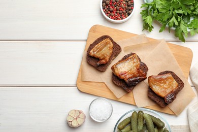 Rye bread with tasty fried cracklings on white wooden table, flat lay. Cooked pork lard