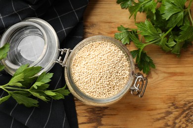 Photo of Dry quinoa seeds in glass jar and parsley on wooden table, top view