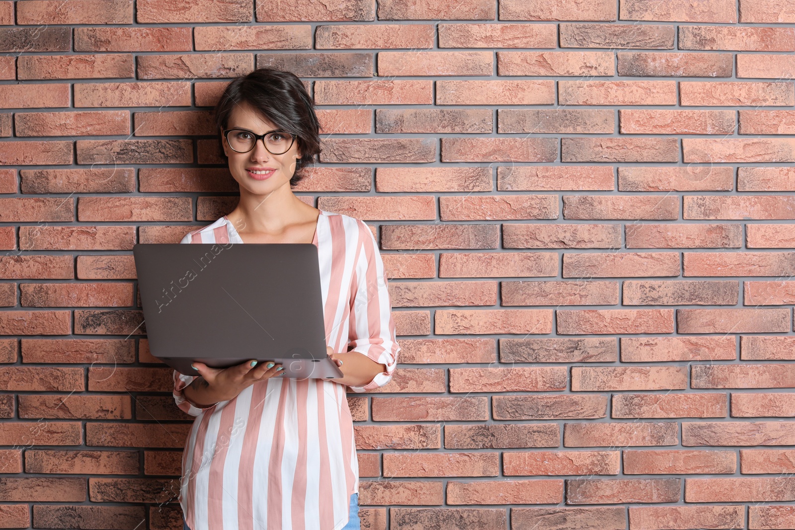 Photo of Young woman with modern laptop on brick wall background