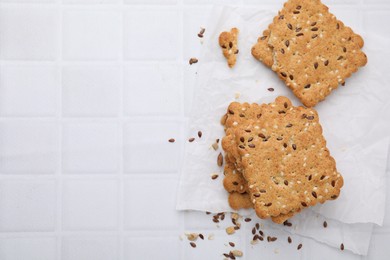 Photo of Cereal crackers with flax and sesame seeds on white tiled table, top view. Space for text