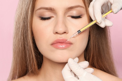 Young woman getting lips injection on color background, closeup. Cosmetic surgery