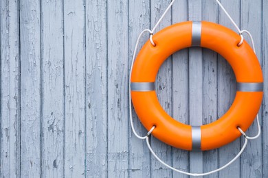 Orange life buoy hanging on light wooden wall, space for text