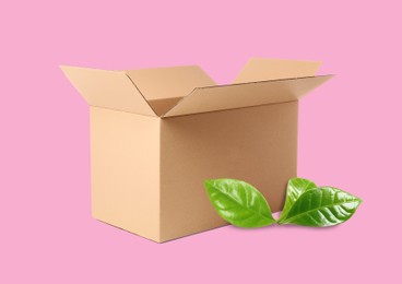 Image of Open cardboard box and green leaves on pink background. Eco friendly lifestyle