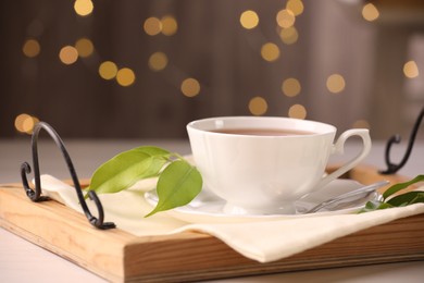 Aromatic tea in cup, saucer, spoon and green leaves on table