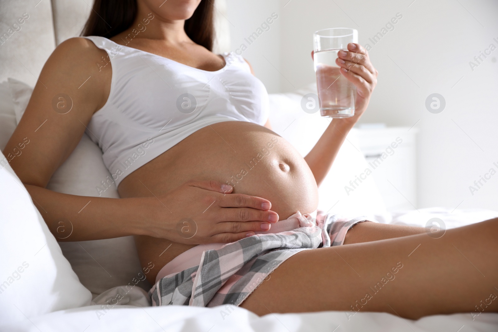 Photo of Young pregnant woman with glass of water in bedroom, closeup. Taking care of baby health