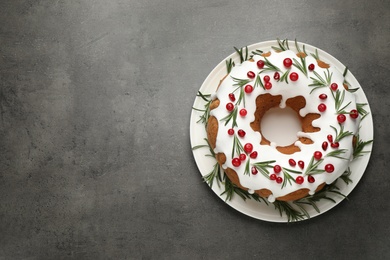 Photo of Traditional Christmas cake decorated with glaze, pomegranate seeds, cranberries and rosemary on grey textured table, top view. Space for text