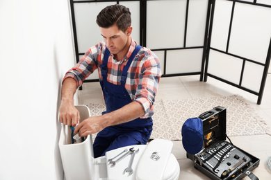 Professional plumber working with toilet bowl in bathroom