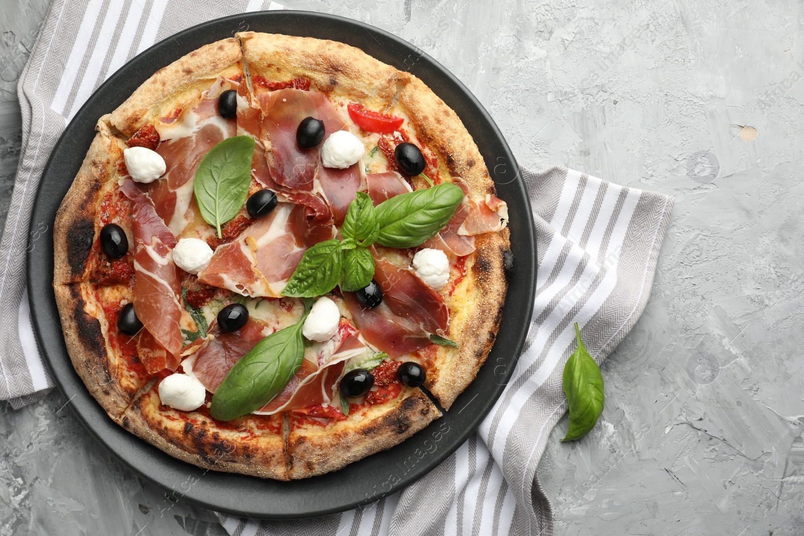 Photo of Tasty pizza with cured ham, olives, mozzarella cheese, sun-dried tomato and basil on gray textured table, top view