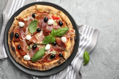 Photo of Tasty pizza with cured ham, olives, mozzarella cheese, sun-dried tomato and basil on gray textured table, top view