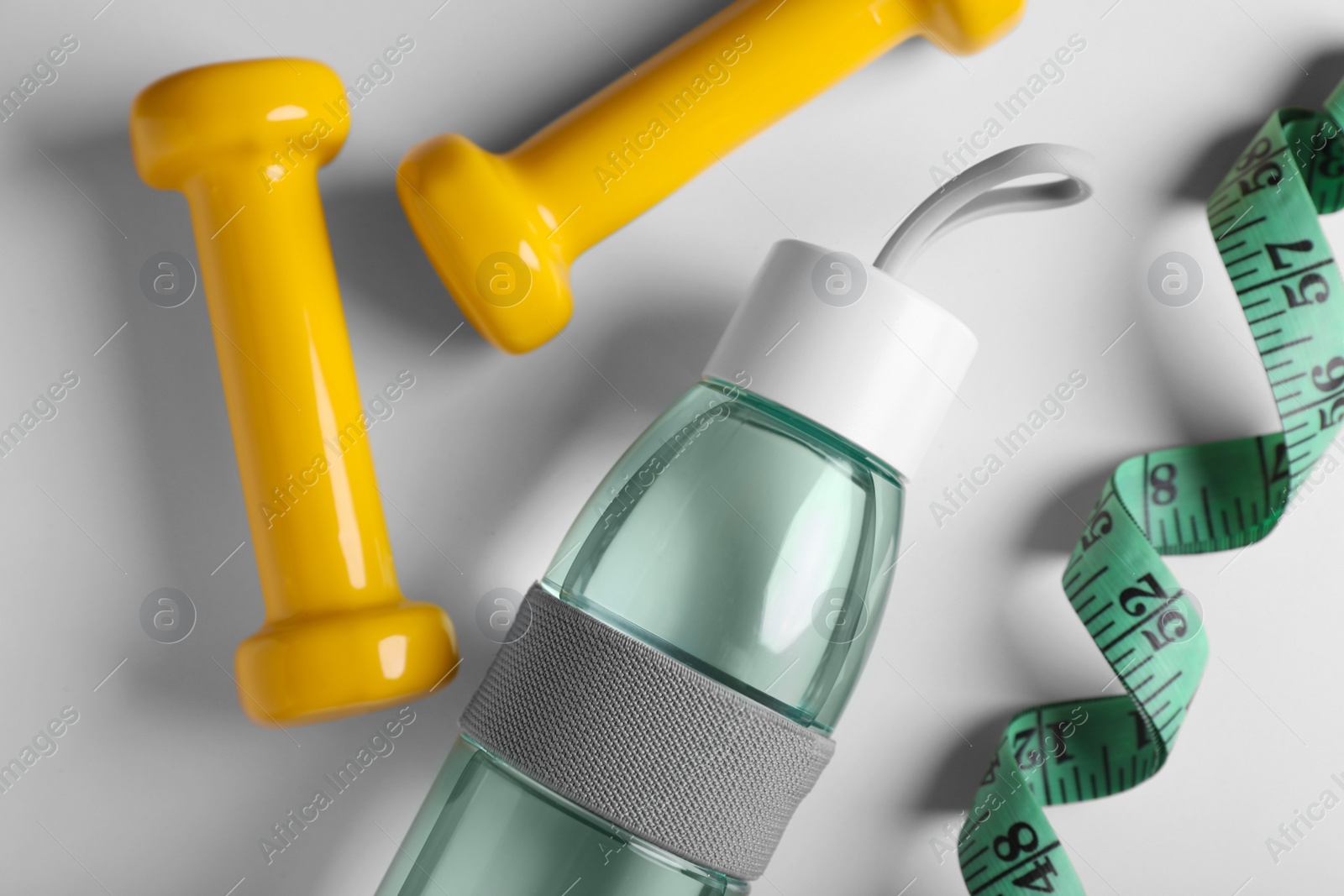 Photo of Measuring tape, dumbbells and bottle with water on white background, flat lay. Weight control concept