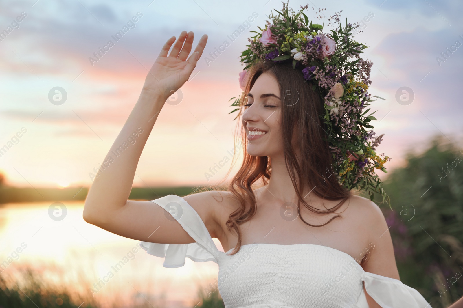 Photo of Young woman wearing wreath made of beautiful flowers outdoors at sunset