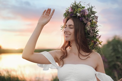 Young woman wearing wreath made of beautiful flowers outdoors at sunset