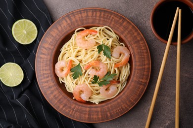 Photo of Tasty spaghetti with shrimps, parsley, lime and soy sauce on brown table, flat lay