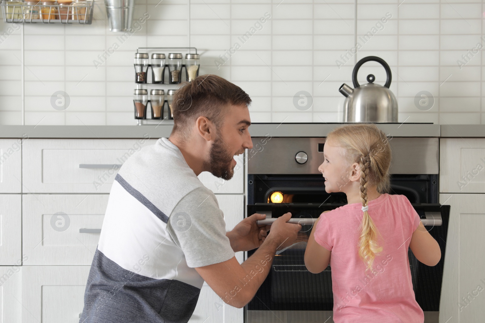 Photo of Father and daughter opening oven while baking in kitchen