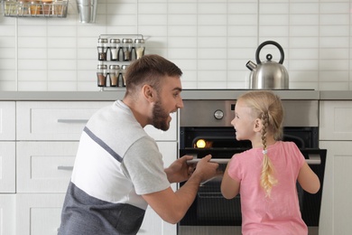 Father and daughter opening oven while baking in kitchen