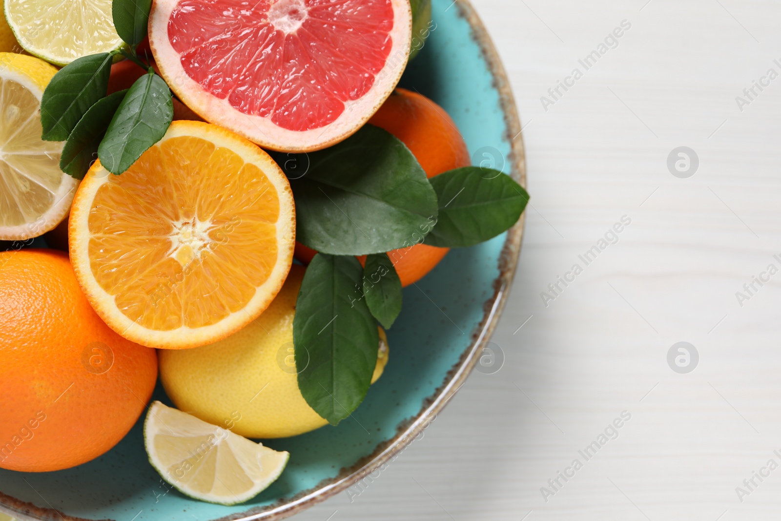 Photo of Different cut and whole citrus fruits on white wooden table, top view. Space for text