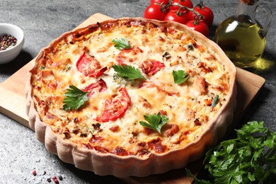Photo of Tasty quiche with tomatoes, parsley and cheese served on grey textured table, closeup