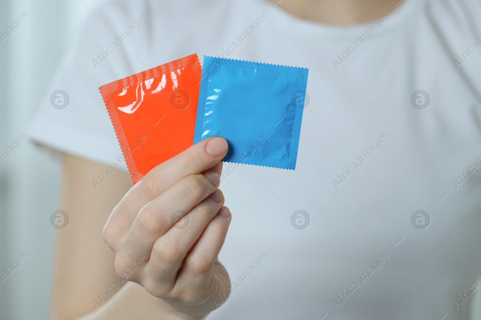 Photo of Woman holding condoms indoors, closeup. Safe sex