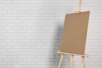 Wooden easel with blank board near white brick wall. Space for text