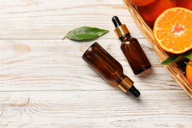 Bottle of tangerine essential oil and fresh fruits on white wooden table, flat lay. Space for text