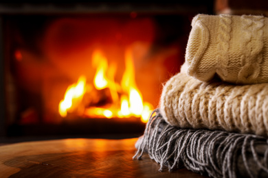 Photo of Stack of knitted clothes and blurred fireplace on background
