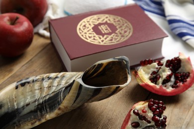 Photo of Shofar, pomegranate, Torah and apples on wooden table, closeup. Rosh Hashanah celebration