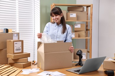 Photo of Post office worker packing parcel at wooden table indoors