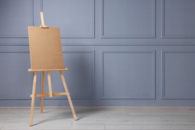Photo of Wooden easel with blank board near grey wall indoors. Space for text