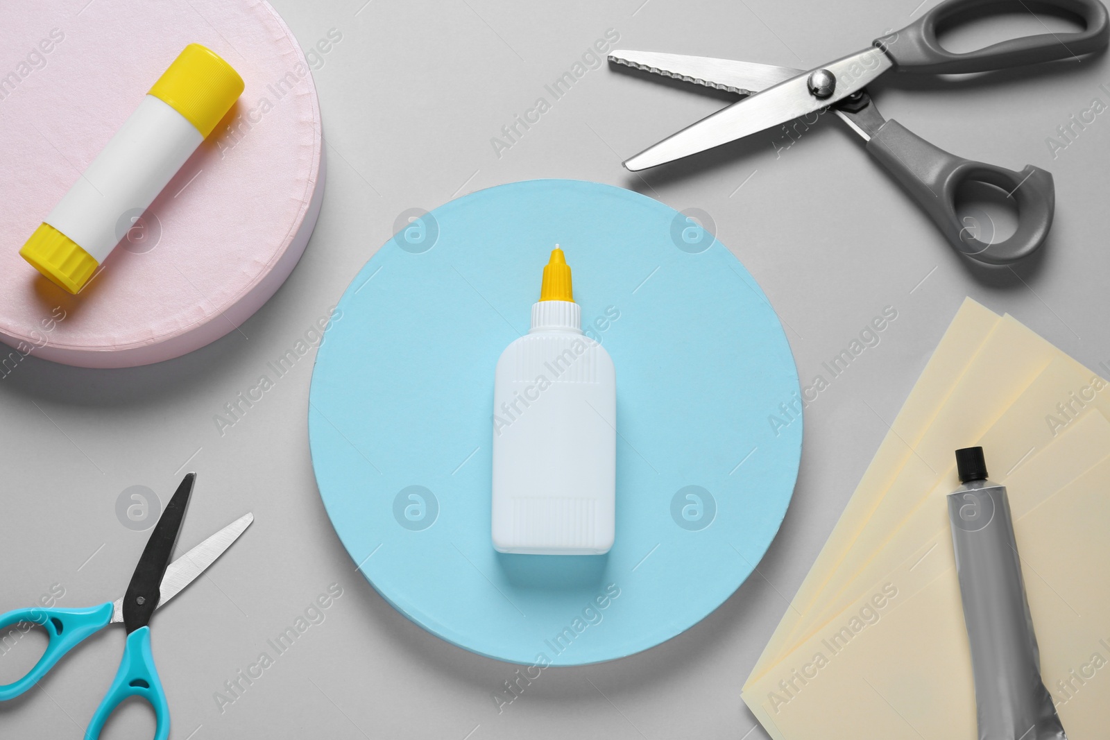 Photo of Different glues and scissors on grey background, flat lay