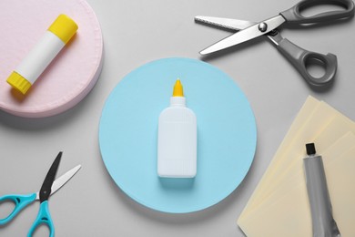 Different glues and scissors on grey background, flat lay