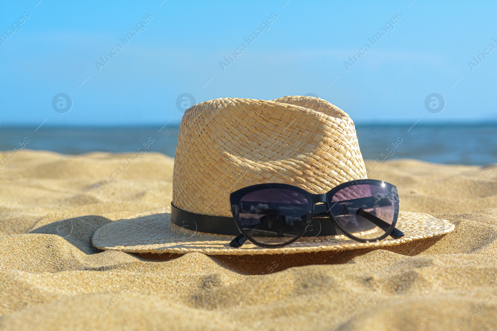 Photo of Hat with beautiful sunglasses on sand near sea