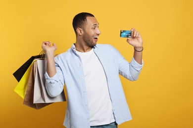 Photo of Happy African American man with shopping bags and credit card on orange background