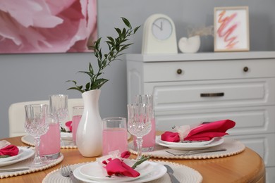 Photo of Color accent table setting. Glasses, plates, vase with green branch and pink napkins in dining room