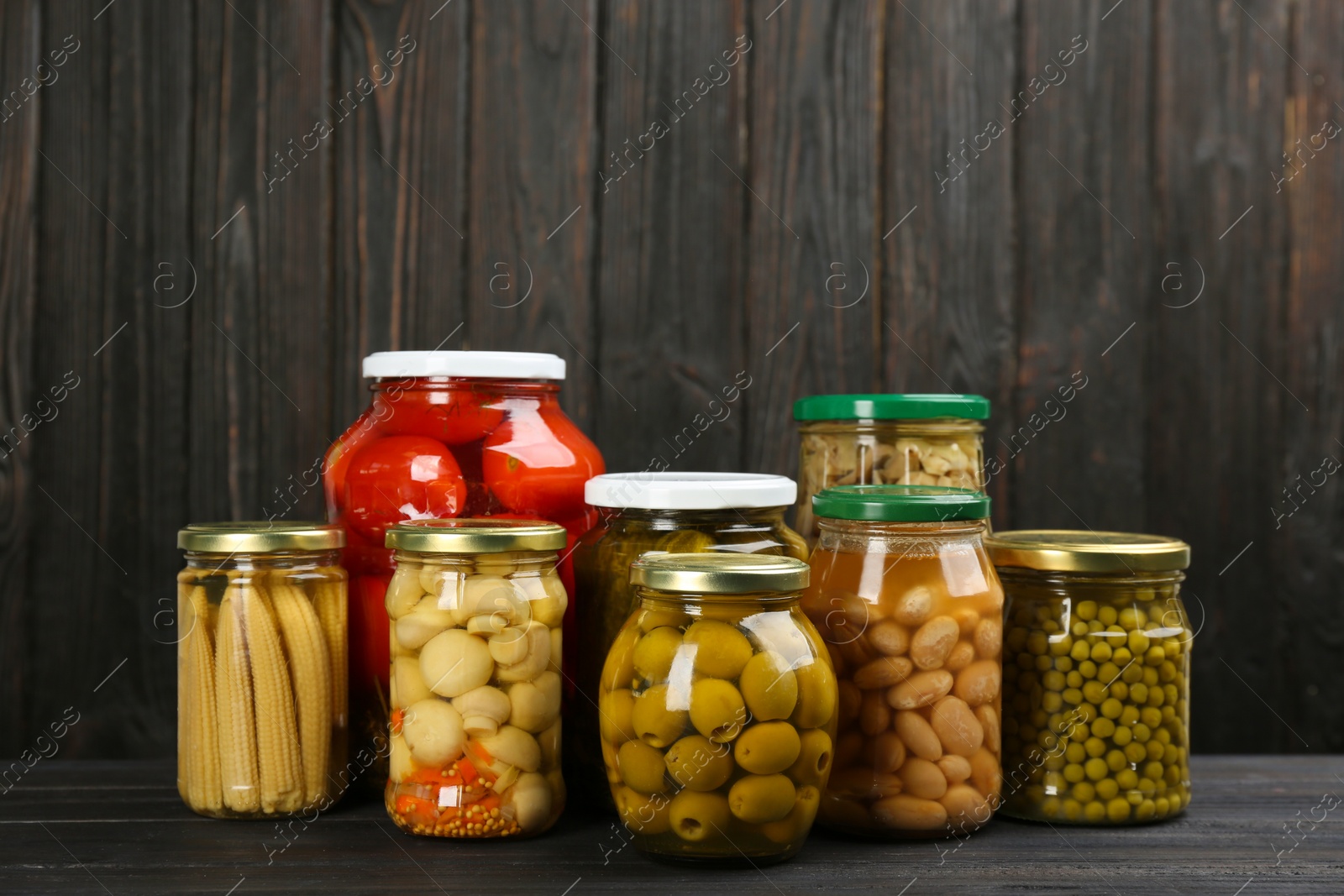 Photo of Glass jars with different pickled vegetables and mushrooms on wooden background