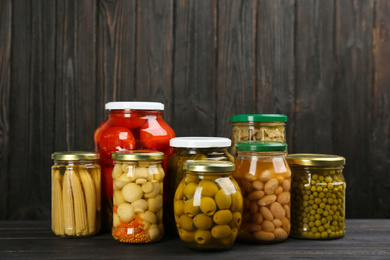 Glass jars with different pickled vegetables and mushrooms on wooden background