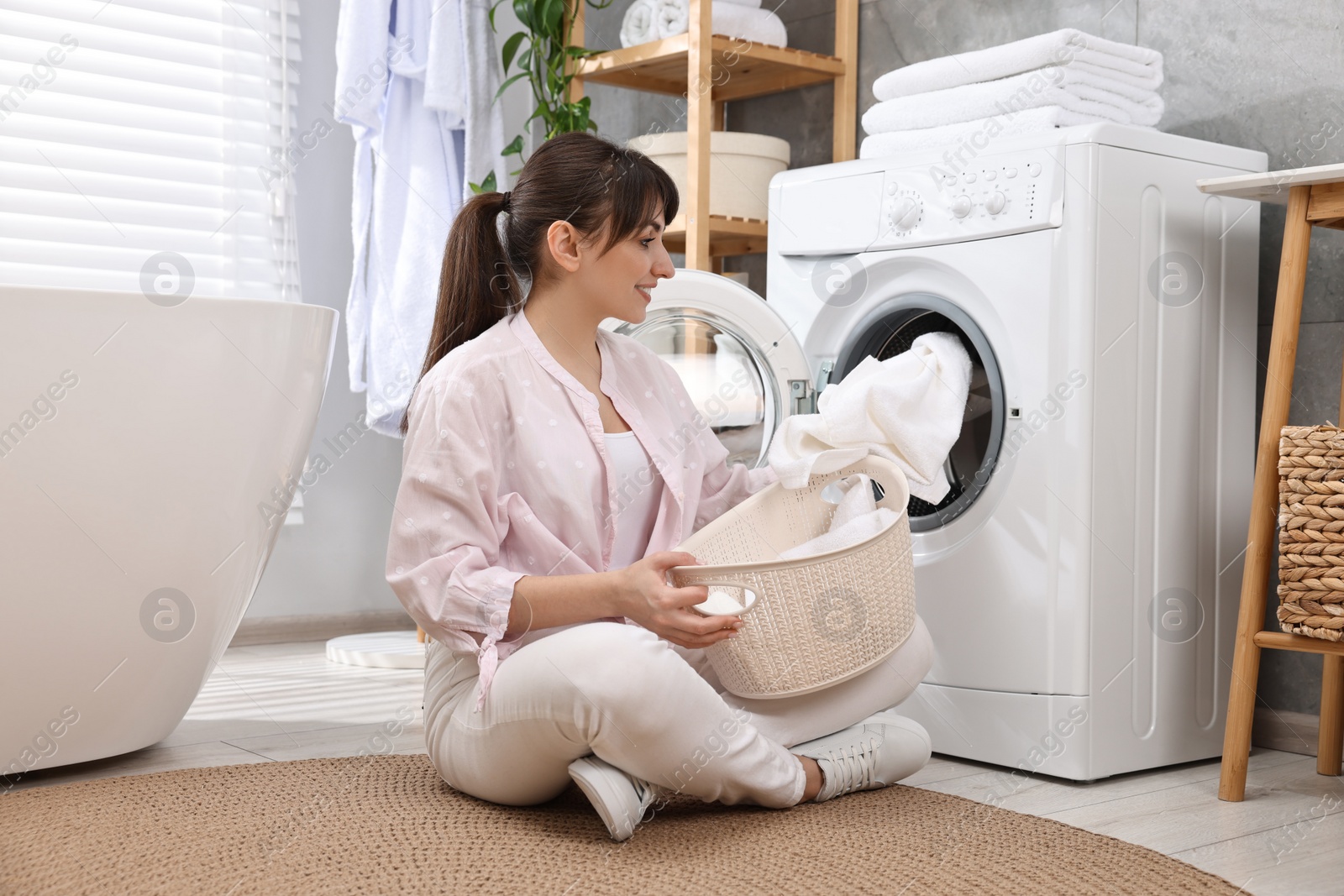 Photo of Happy young housewife putting laundry into washing machine at home