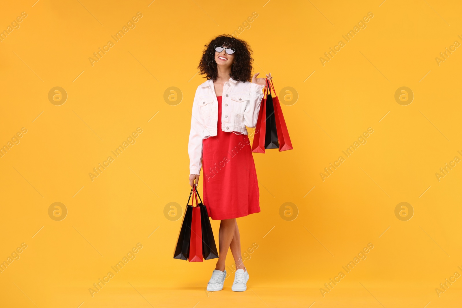 Photo of Happy young woman with shopping bags and stylish sunglasses on yellow background