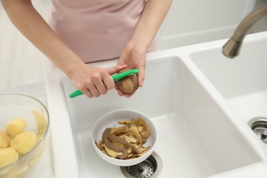 Photo of Woman peeling potato near kitchen sink, closeup. Preparing vegetable