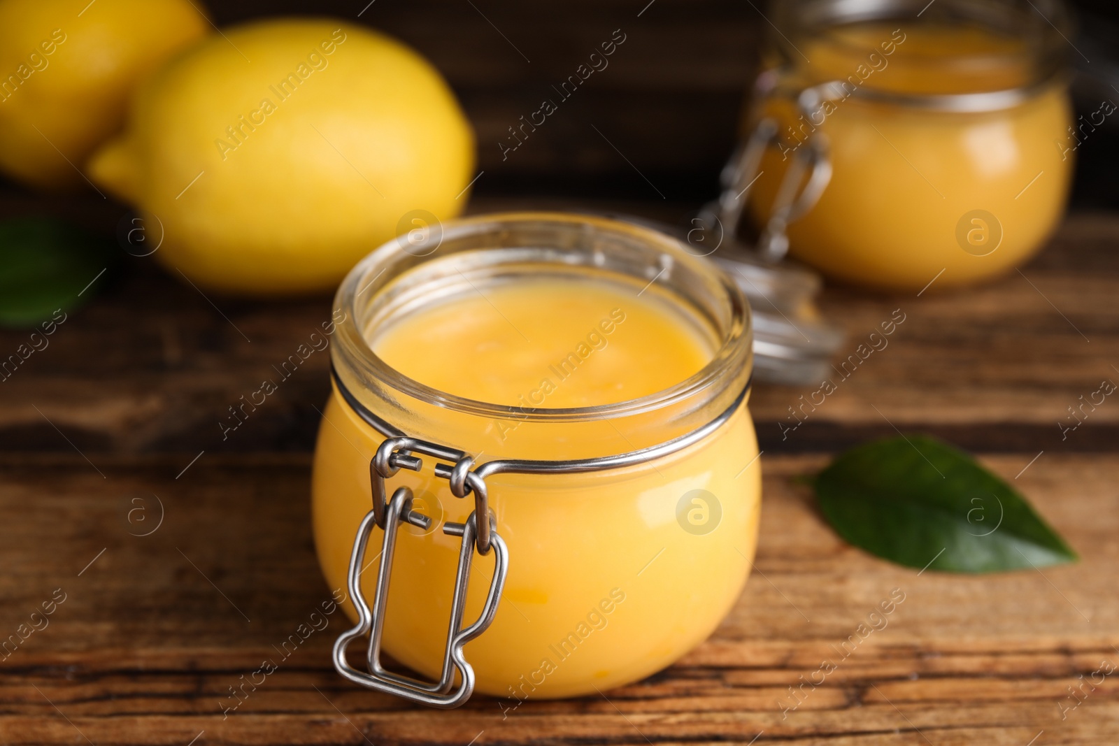 Photo of Delicious lemon curd in glass jar on wooden table