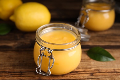 Photo of Delicious lemon curd in glass jar on wooden table