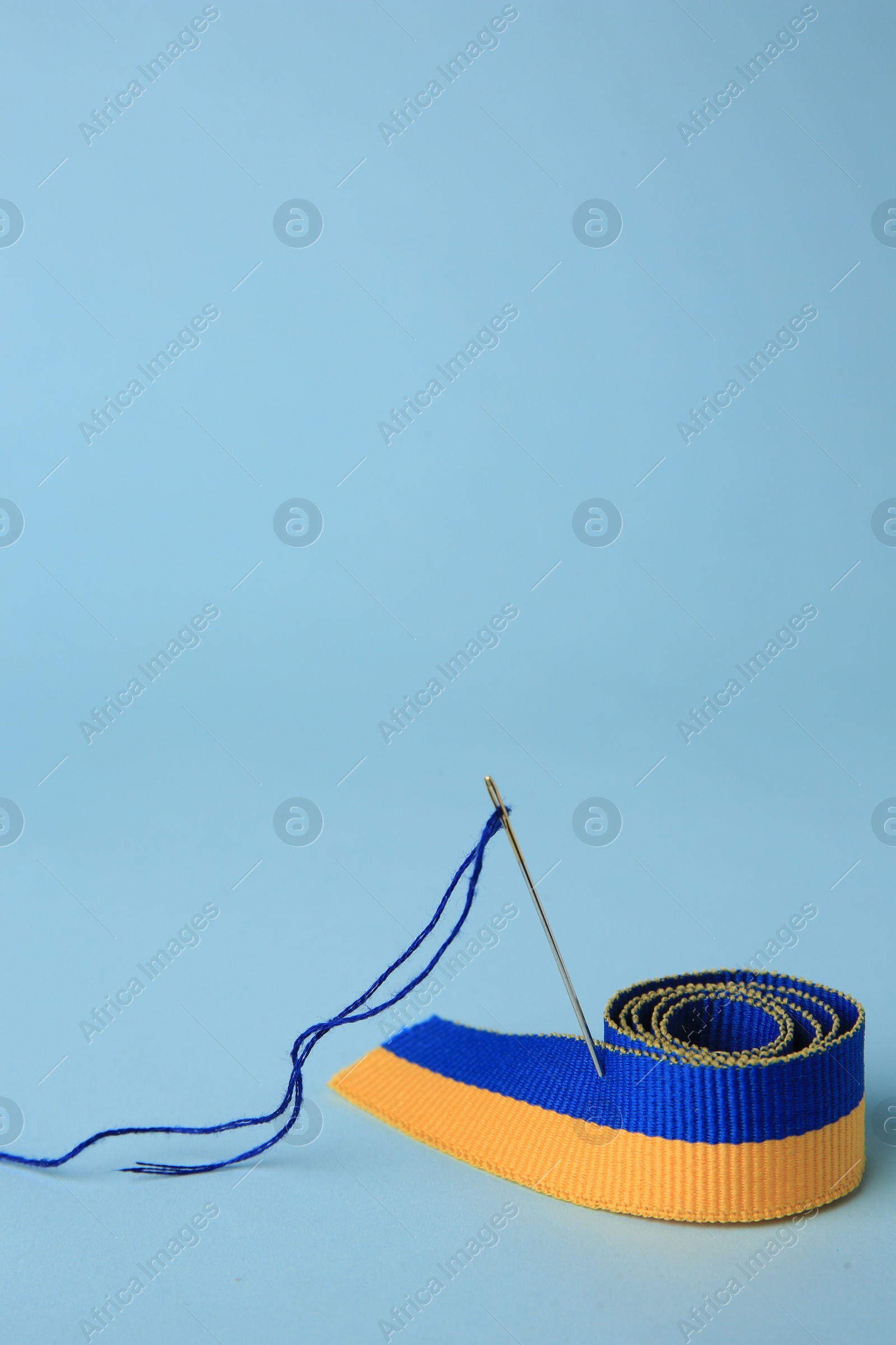 Photo of Sewing needle with thread and color ribbon on light blue background