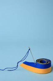 Photo of Sewing needle with thread and color ribbon on light blue background
