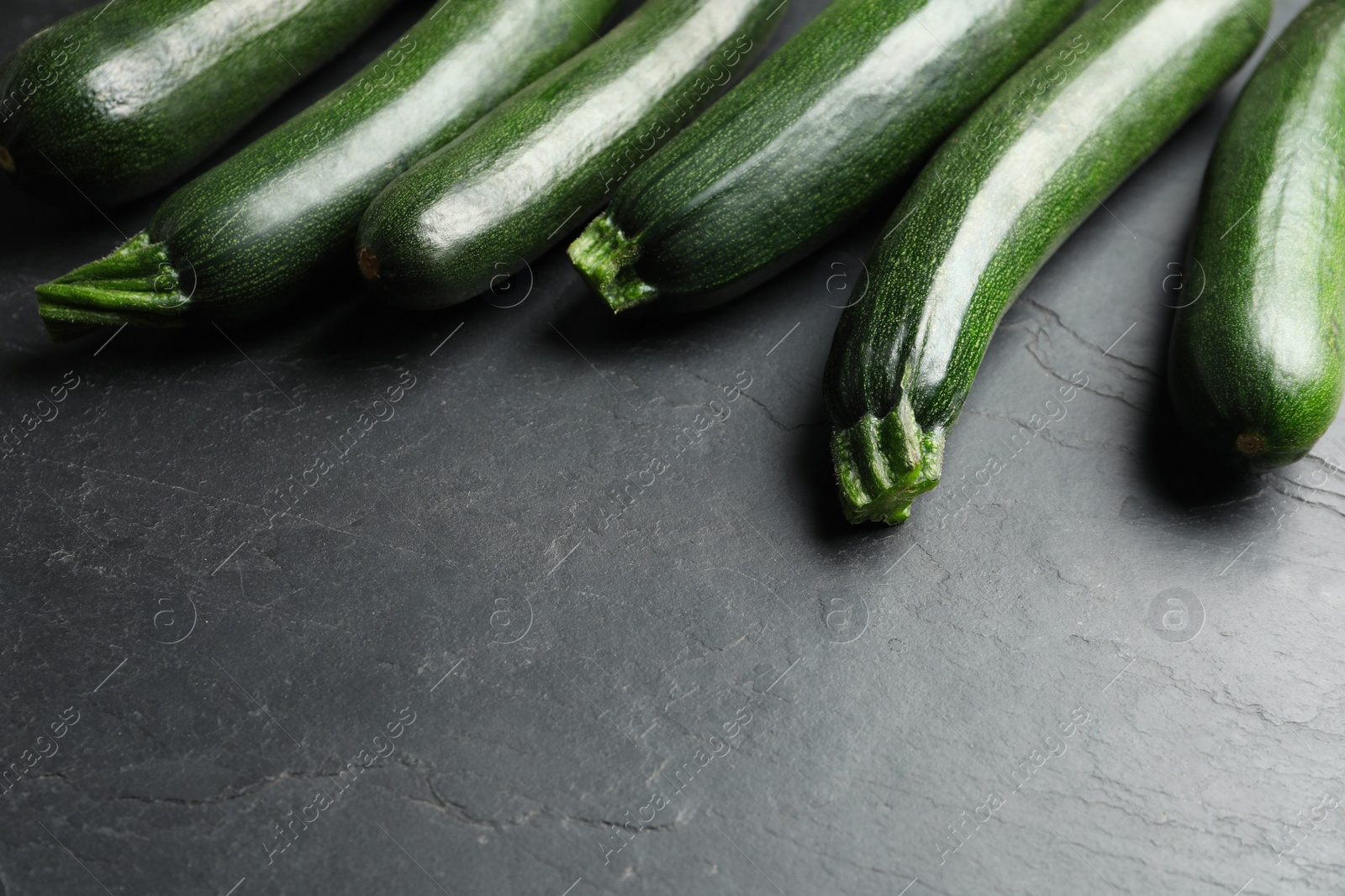 Photo of Green ripe zucchinis on black slate table. Space for text