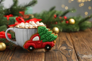 Photo of Tasty Christmas cookie in shape of car with fir tree, cocoa with marshmallows and festive decor on wooden table, closeup. Space for text