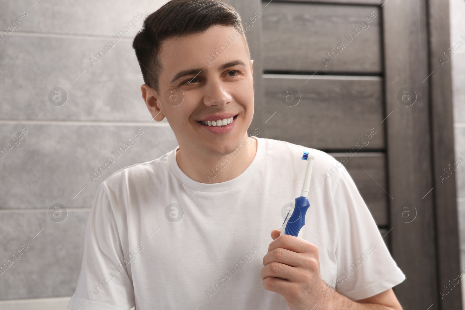 Photo of Happy man with electric toothbrush in bathroom