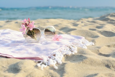 Beautiful sunglasses with tropical flower on blanket near sea. Space for text