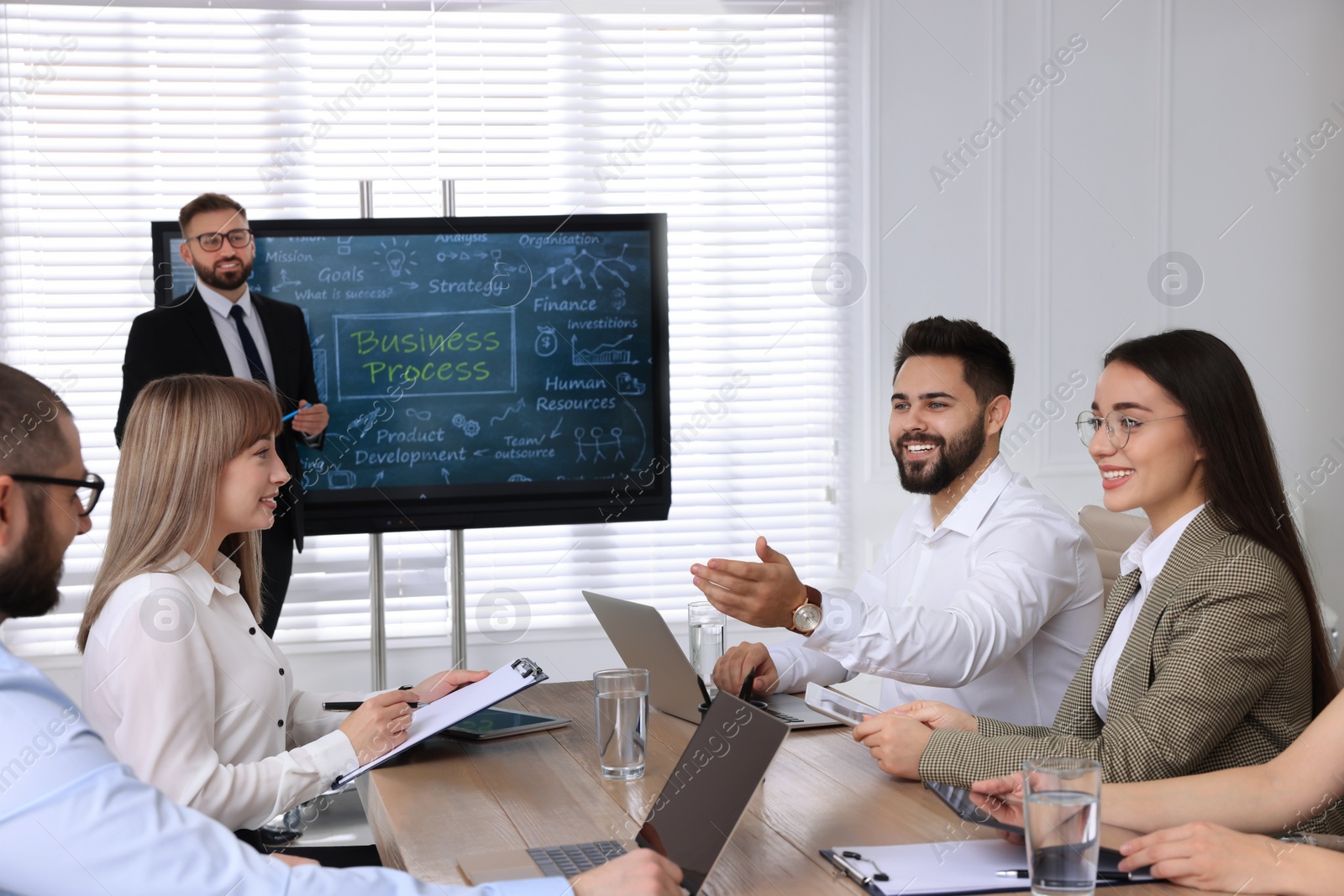 Photo of Business trainer near interactive board in meeting room during presentation, focus on colleagues