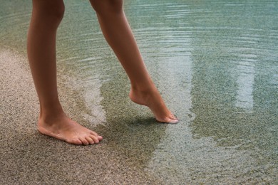 Photo of Child testing sea water temperature with foot on beach, closeup
