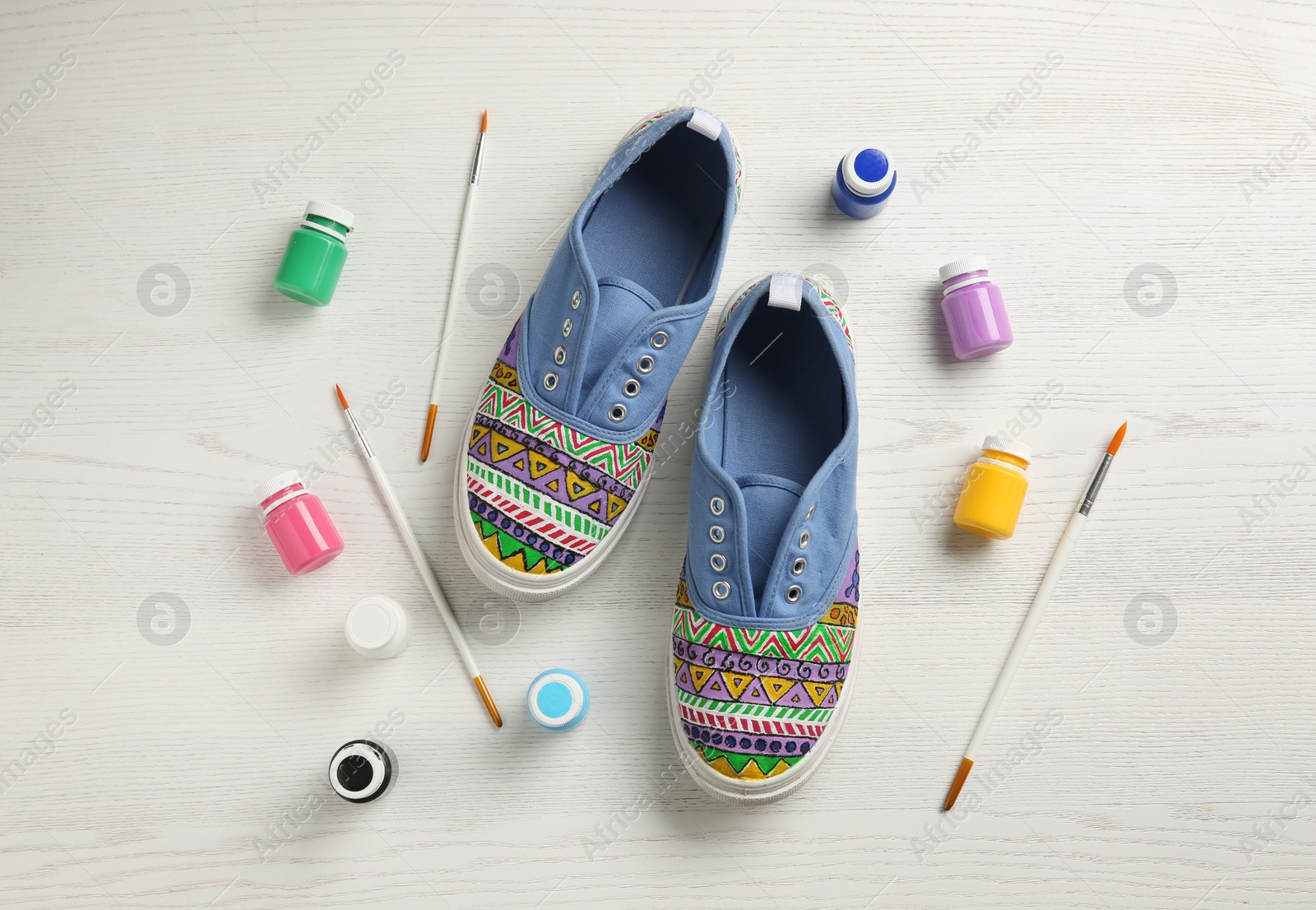 Photo of Amazing customized shoes and painting supplies on white wooden background, flat lay